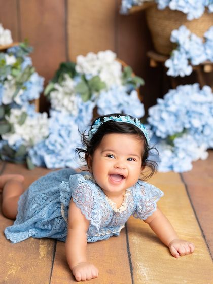 A happy crawl on a rustic wooden floor. This baby girl's joyful expression and the surrounding blue flowers make for a delightful milestone photo.