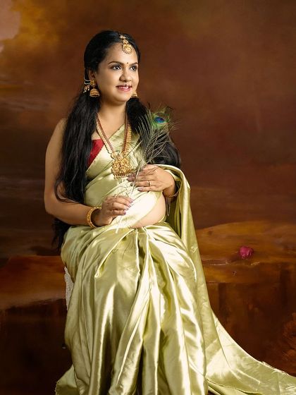 A regal portrait of a mom-to-be in a light green silk saree, holding a peacock feather, symbolizing beauty and new life.