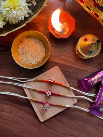 These delicate floral rakhis are handmade with thread and small beads. They come in a variety of warm colors like orange, pink, and red.