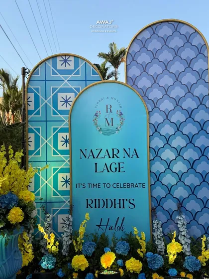 A custom "Nazar Na Lage" sign for the Haldi ceremony, designed with beautiful typography and set against a backdrop of blue and yellow patterns.