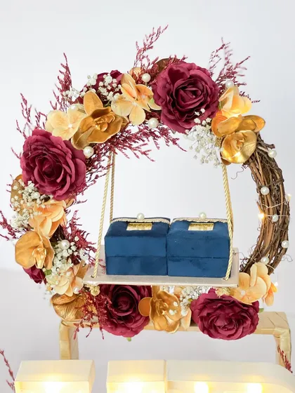 A close-up of our floral wreath ring platter. The rings are presented on a delicate swing, surrounded by rich burgundy and gold flowers for a touch of romance.