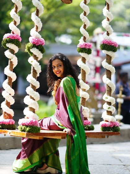 A stunning portrait of a woman in a traditional saree, sitting on a beautifully decorated floral swing.