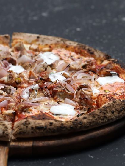 The Bird in Hand pizza, cut and ready to serve. You can see the combination of roasted chicken, onions, and dollops of blue cheese on a beautifully baked crust.
