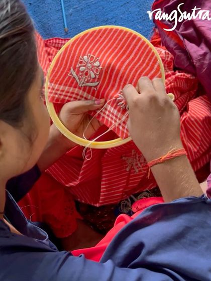 A close-up of an artisan working on a Chikankari saree. The combination of the striped handloom fabric and the delicate white embroidery creates a stunning contrast.
