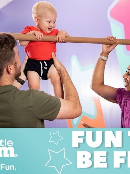 Our instructors work alongside parents to ensure every child gets the support they need. Here, a parent and instructor team up to help a baby practice standing on the bar, an exercise that builds leg strength and balance.