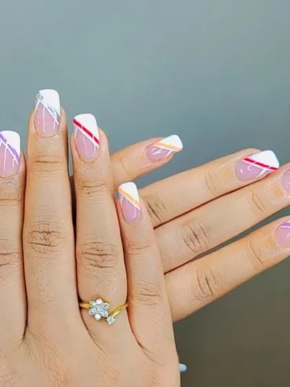 A colorful and graphic design with white French tips accented by intersecting colored and silver glitter lines.