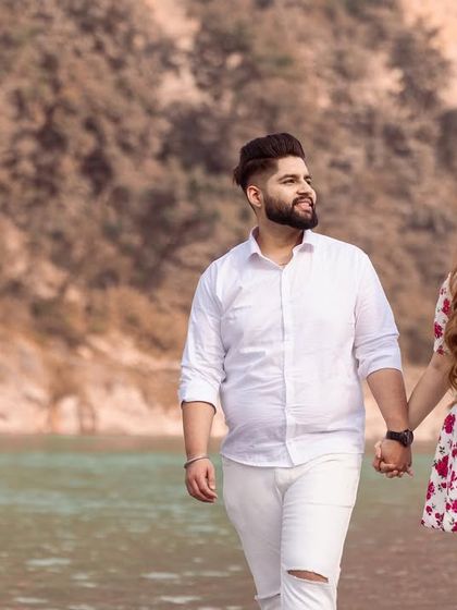 A classic walking shot of the couple hand-in-hand by the river, showcasing their connection and the beautiful scenery.