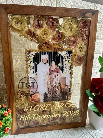 A clear, frontal view of the large teakwood frame, showing the arrangement of the preserved pink and white roses.