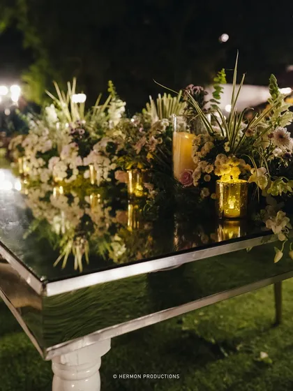 A mirrored tabletop reflecting the floral centerpieces and candlelight, a sophisticated detail for an evening reception.