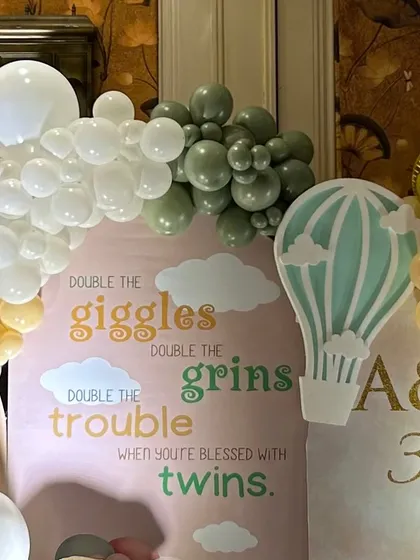 A section of the backdrop for the twins' party, featuring a hot air balloon graphic and the sweet phrase, "Double the giggles, double the grins".