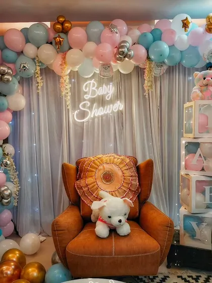 An elaborate baby shower decoration for a living room, featuring a full balloon arch, a neon sign, 'BABY' blocks, and teddy bear props.