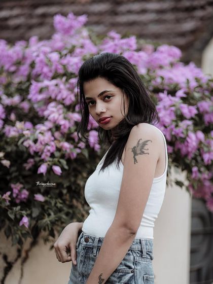 A cool and casual portrait against a wall of purple flowers. The contrast between the simple outfit and the vibrant background makes the image pop.