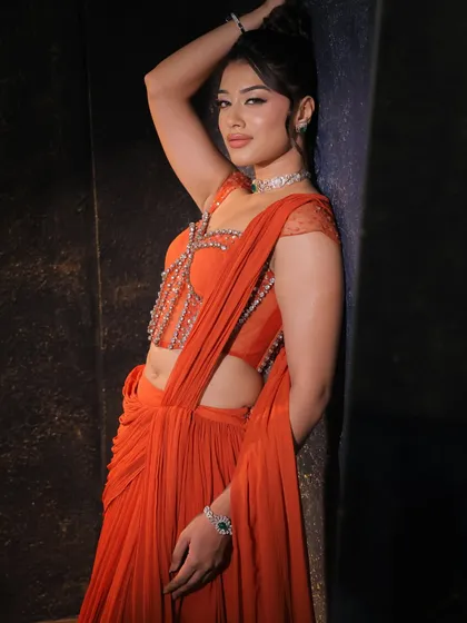 An artistic pose in the orange corset saree, highlighting its vibrant color and the way the light catches the embellishments on the structured bodice.