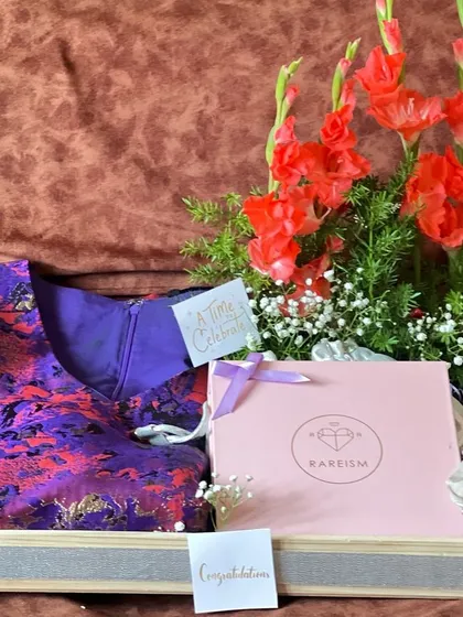 An elegant engagement gift hamper featuring a beautiful dress, fresh gladiolus flowers, and other curated items. This is a wonderful way to congratulate a newly engaged couple.