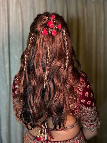 A beautiful half-up style for a bride, featuring a braided bun, cascading pearl strings, and fresh red flowers.
