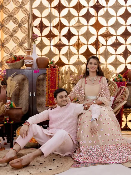 For a village-themed event, we chose this beautiful beige and red lehenga. The couple looks perfectly coordinated, sitting in a rustic setting that complements their outfits.