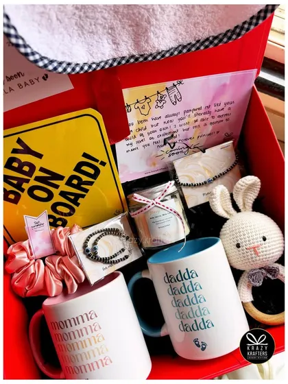 A vibrant red hamper for the parents-to-be, featuring 'Momma' and 'Dadda' mugs, a custom bib, a 'Baby on Board' sign, and other essentials.