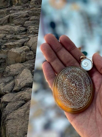 A hand holding an antique pendant with intricate calligraphy.