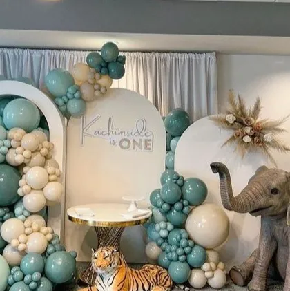We bring wild adventures to life with our themed parties. This immersive jungle safari setup for a first birthday features lifelike animal props like a giraffe and elephant, set against custom arched backdrops and a lush balloon arrangement in sage green and neutral tones.