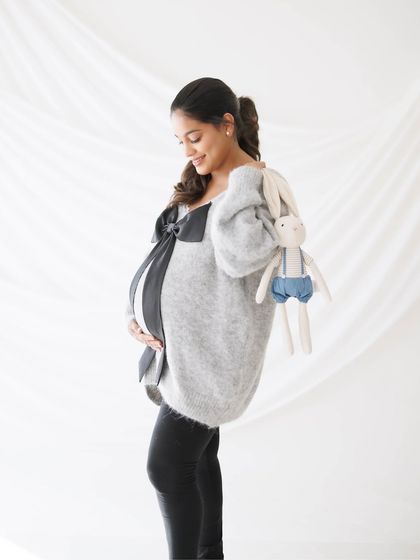 A smiling, happy portrait of a mother-to-be in a cozy sweater, holding a stuffed bunny, full of sweet anticipation.