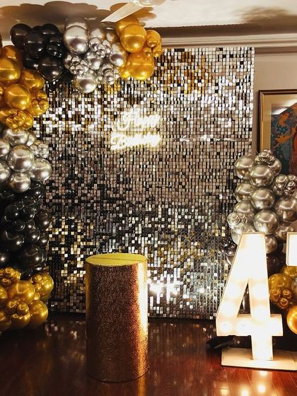 Turning 47 with sparkle and shine. We designed this glamorous setup with a silver sequin wall, large "47" marquee numbers, and a dramatic balloon arrangement in black, gold, and silver chrome for a truly dazzling birthday bash.
