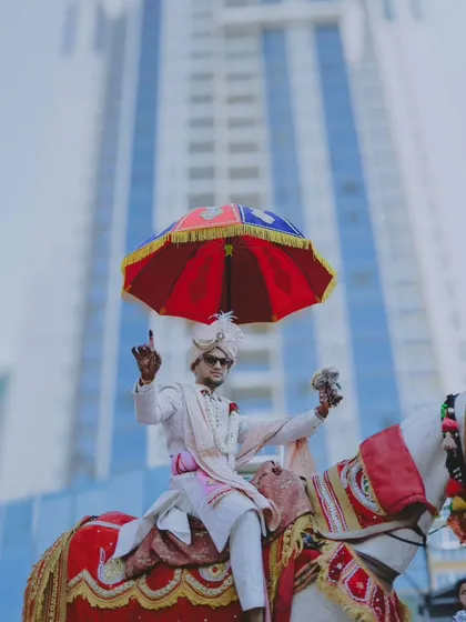 The groom's grand arrival on a decorated horse for the baraat, set against a modern city backdrop.
