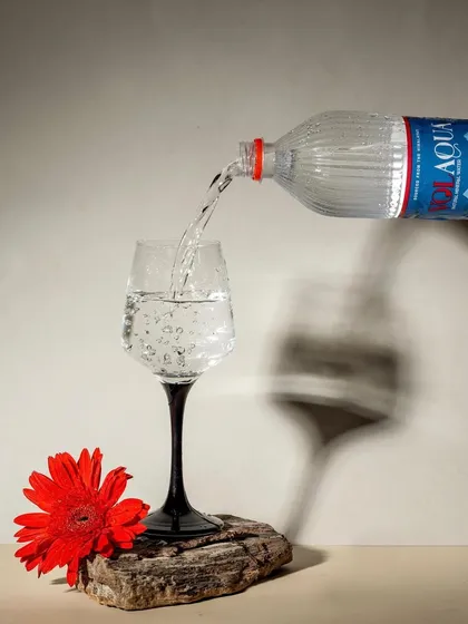 An artistic shot of Volaqua water, using strong shadows and a single red flower to create a dramatic composition. This style elevates a simple product into a piece of art.
