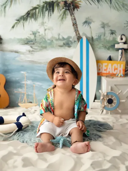 A happy baby boy in a beach-themed setup, looking up with a joyful expression. These themed shoots are perfect for milestone celebrations.