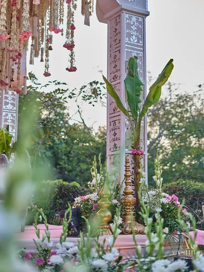 A close-up of the mandap's details, showing the traditional brass decor, fresh white tuberoses, and the intricately patterned pillar next to a sacred banana leaf.
