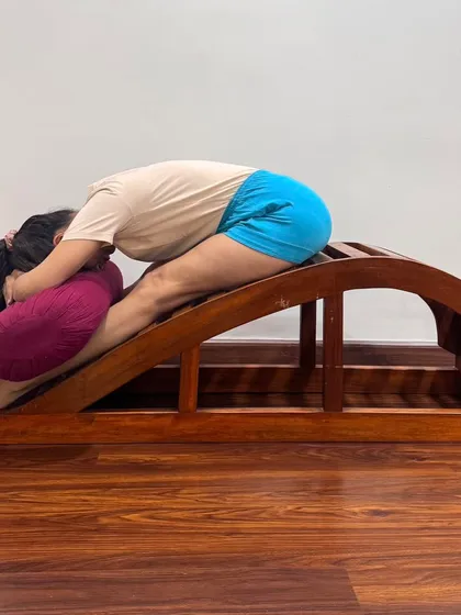 For those with stiff backs, the backbend bench makes forward bends more accessible. This variation of Janu Sirsasana provides a progressive stretch, making the spine supple and teaching the brain to remain alert even in a state of surrender.