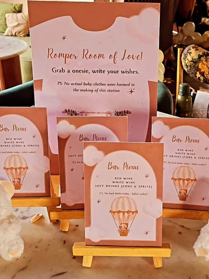 A creative 'Romper Room of Love' station at a baby shower. Guests can write wishes on onesies, a fun and interactive activity. The teddy bear and hot air balloon theme is seen in the stationery.