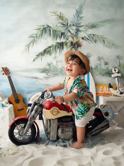 A happy toddler pretends to ride a miniature motorcycle in a fun, beach-themed studio session.