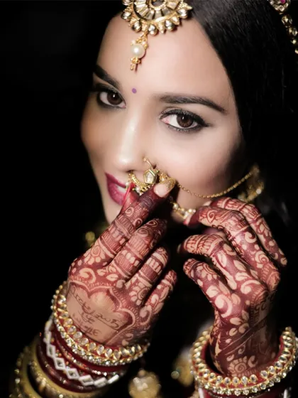 A bridal portrait that focuses on the intricate details. From the delicate mehndi design on her hands to the traditional nath and sparkling bangles, every element of the bride's look is highlighted with artistic lighting.
