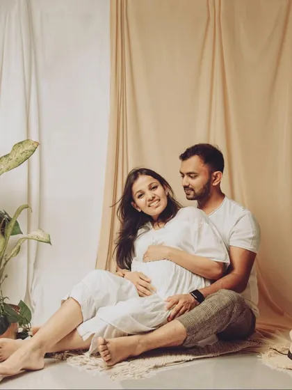 Dressed in simple whites against an earthy, neutral backdrop, this portrait captures a serene and natural moment of togetherness for the expecting couple.