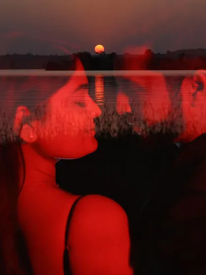 A creative double exposure combining a sunset over water with a close-up of the couple, bathed in red light for an abstract, artistic feel.