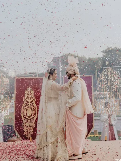 A beautiful varmala exchange on a stage covered in rose petals. The moment is made even more dramatic with cold pyros and a backdrop of royal red banners.