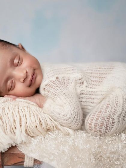 Our sweetest little boy, with the most precious smile. This simple pose on a soft blanket highlights the pure joy of a sleeping baby.