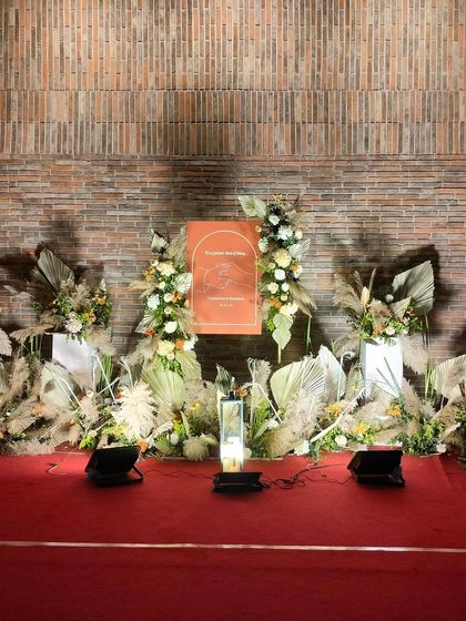 For this engagement, we created a boho-chic stage against a rustic brick wall. The design features dried pampas grass, palm leaves, and fresh white and yellow flowers, creating a beautiful texture-rich backdrop.