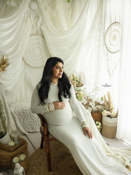 A graceful seated portrait of a mother-to-be. The flowing white gown and the dreamy, light-filled background create an ethereal and elegant image.