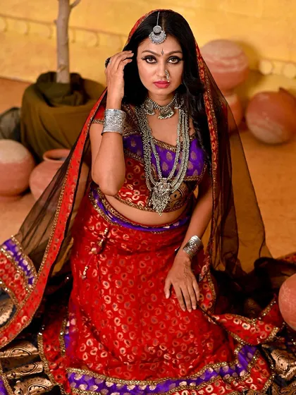 A kneeling pose from the Rajasthani series, showcasing the full, vibrant ghagra. The black veil adds a layer of mystery and tradition to the look.