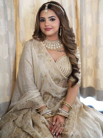 A seated portrait of the bride in the ivory and gold lehenga, offering a detailed view of the heavy choker and bangles.