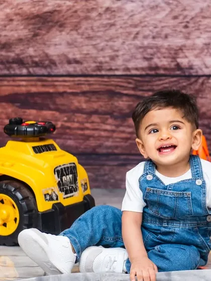 A happy baby boy in denim overalls enjoying his construction-themed pre-birthday photoshoot.