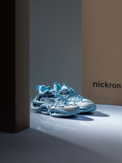 These futuristic blue sneakers are placed in a clean, architectural setting with the brand's packaging, creating a cool and modern product shot.