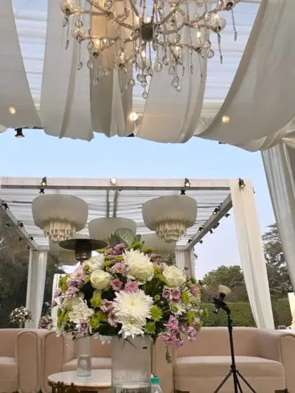A lounge area at an ivory themed wedding, featuring elegant seating under a canopy of draped fabric and crystal chandeliers.