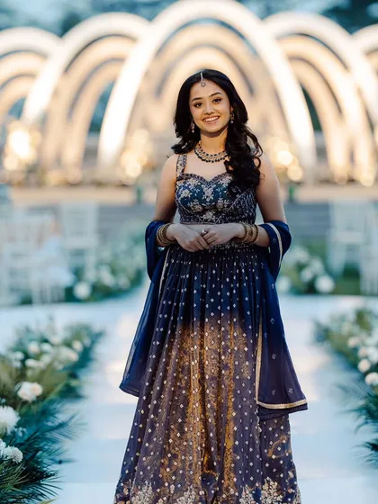 The bride looking radiant at her Roce ceremony. She stands before the aisle of modern white arches, which are beautifully lit to create a grand and elegant atmosphere.