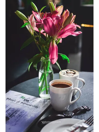 A quiet coffee moment in a cafe, with two mugs set against a dark table. The composition with flowers and a menu creates a realistic and inviting scene.