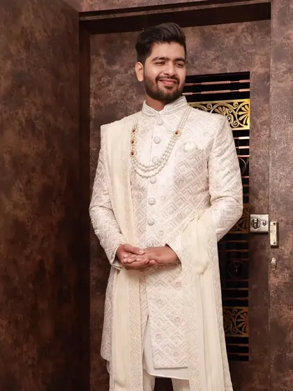 A full-body shot of the groom in a classic ivory sherwani. The natural makeup and clean hairstyle complete this elegant and traditional wedding look.