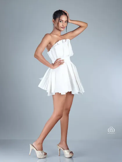 A full-length shot of the model in the paper dress, showcasing its sculptural quality. The clean studio background keeps the focus on this unique, wearable art piece.