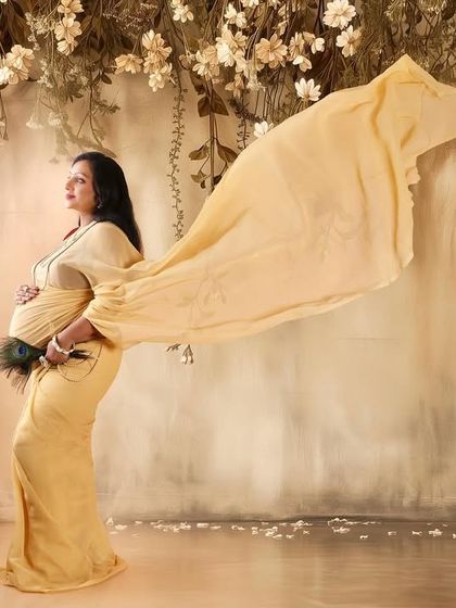 A beautiful solo portrait from the same traditional session. The golden saree's fabric is tossed for a flowing, dynamic effect against a floral backdrop.