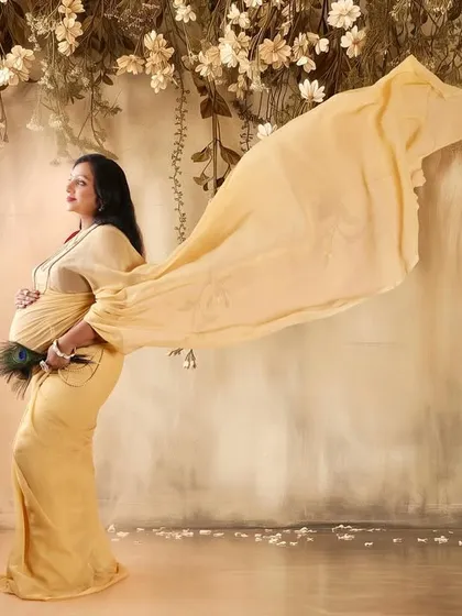 A beautiful solo portrait from the same traditional session. The golden saree's fabric is tossed for a flowing, dynamic effect against a floral backdrop.